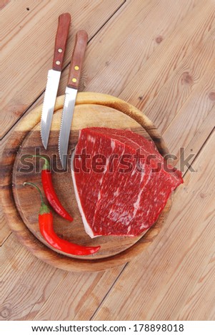 fresh raw beef meat steak chunk with red hot pepper on wood with stainless steel knife