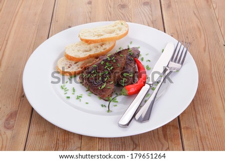 fresh hot grilled beef meat steak served with red hot pepper and white bun slices on plate over wooden table