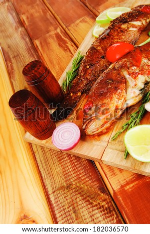 healthy food: two fried sea bass fish served with tomatoes and vegetables on big wooden board over table