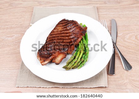 meat table : grilled beef fillet with asparagus served on white plate with cutlery over wooden table