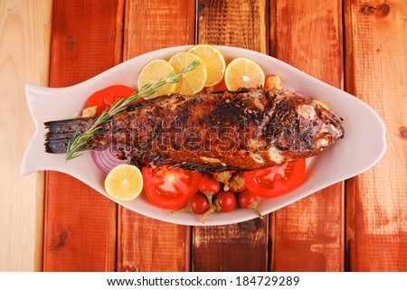 healthy lunch : whole fried sea sunfish on wooden table with lemons peppers and tomatoes and rosemary twig