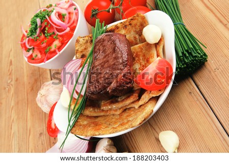 grilled meat : beef ( pork ) garnished with tomatoes salad in bowl , green chives , and tomatoes on side on wooden table