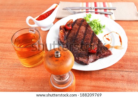 rural design new york meat style beef steak fillet on white plate with hot chili pepper served with tea cup ketchup in Gravy boat pepper mill and cutlery on napkin on wooden table