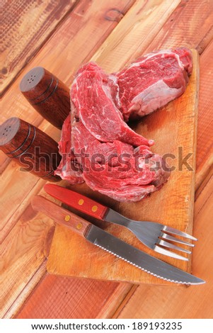 fresh raw uncooked beef fillet mignon entrecote on board prepared for cooking on wood table with cutlery and castors