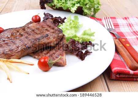 meat food : roast steak boneless with roast onion and red hot peppers, served on green lettuce salad on dish isolated over wooden table