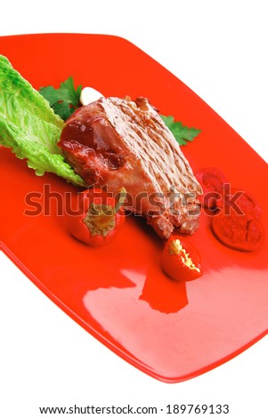 meat food : roast beef garnished with green lettuce and red chili hot pepper on red plate isolated over white background