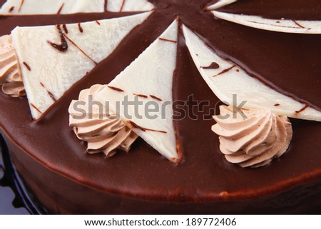chocolate cream brownie cake topped with white chocolate slice and cream flowers on black plate isolated over white background