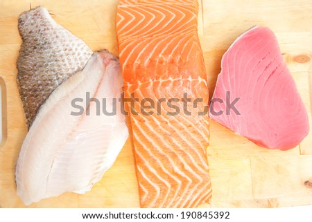 raw set of sea fish food : salmon , red tuna, and sole fish chunks served on wooden plate isolated on white background