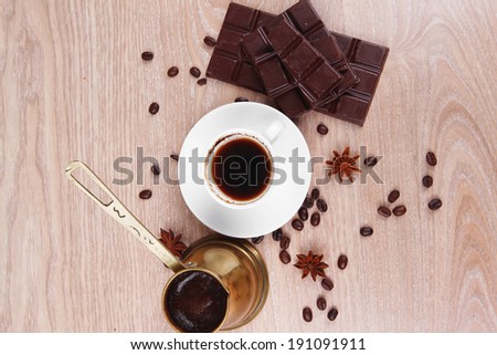sweet hot drink : black Turkish coffee in small white mug with coffee beans spilled on a wooden table with stripes of dark chocolate and copper Arab Cezve full coffee