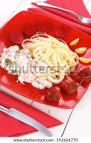 mediterranean cuisine: fresh rose wild salmon baked in cream cheese sauce with italian pasta and red hot pepper on plate over white wooden table with vegetable salad