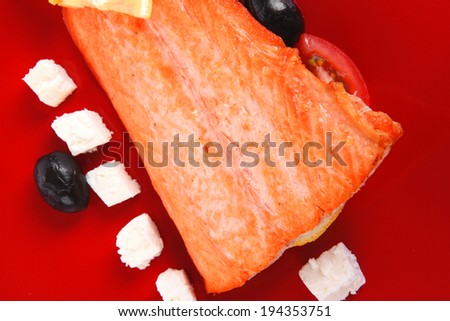 roast salmon fish meat fillet with lemon black greek olives white goat cheese on red plate isolated over white background