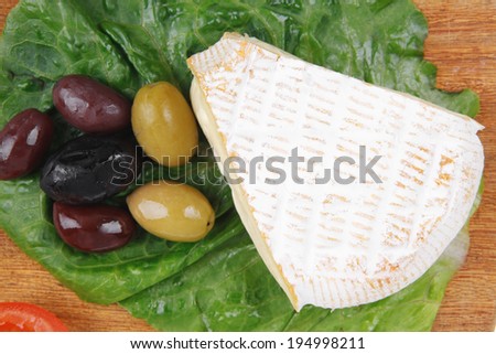 aged camembert cheese on wooden platter with olives and tomato isolated over white background