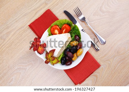aged brie cheese on salad in white dish over red cloth on with olives and tomato over wooden table