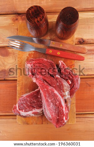 fresh raw uncooked beef fillet mignon entrecote on board prepared for cooking on wood table wtih cutlery and castors