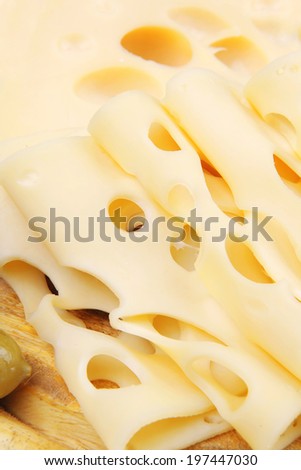 yellow swiss cheese sliced on wooden platter with olives and tomato isolated over white background
