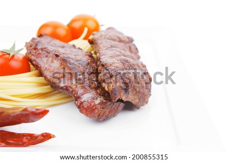 grilled beef fillet with pasta and tomatoes on white plate isolated over white background