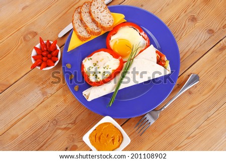 fried eggs and tortilla with salad , red hot pepper and mustard, served on blue plate with cutlery over wooden table in restaurant