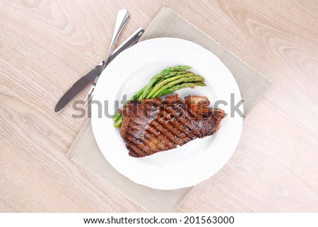 meat table : rare medium roast beef fillet with asparagus served on white plate with cutlery over wooden table