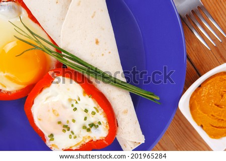 fried eggs and tortilla with salad , red hot pepper and mustard, served on blue plate with cutlery over wooden table in restaurant