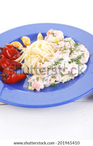 fresh rose wild salmon baked in cream cheese sauce with italian pasta and red hot pepper on blue plate over white wooden table with vegetable salad