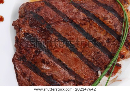 fresh rich juicy grilled beef meat steak fillet with marks on white plate over wooden table decorated with sauces and cutlery new york style