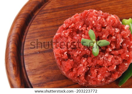 very big raw hamburger cutlet with sprouts and chilli pepper on wooden plate isolated over white background