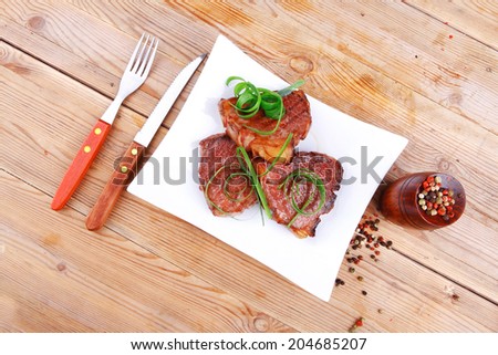 roasted beef meat strips steak on white ceramic plate with hot dry pepper on wood table