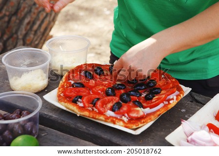 prepare hand made pizza with olives and tomatoes on wooden table on picnic with different kind of cheeses