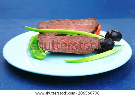 meat food : roasted fillet mignon on blue plate with pepper tomatoes and black greek olives over blue wooden table