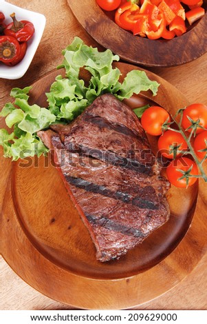 fresh rich juicy grilled beef meat steak fillet with marks on wooden plate over table decorated with lettuce salad and cutlery, new york styled cuisine