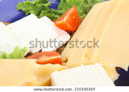 set of gourmet cheese slice and chunk ( bar)  white goat greek yellow french aged on half of rye bread on green lettuce salad with tomatoes on blue plate isolated over white background