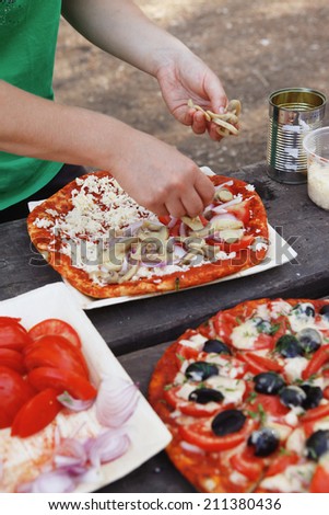 making hand made pizza with olives and tomatoes on wooden table on picnic