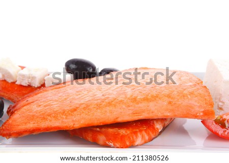 fresh grilled salmon meat fillet with goat light greek feta cheese black olives and tomatoes over long white plate isolated on white background