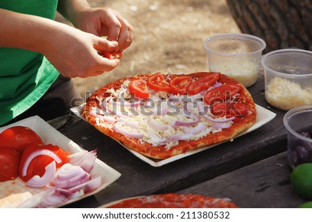 making hand made pizza with olives and tomatoes on wooden table on picnic