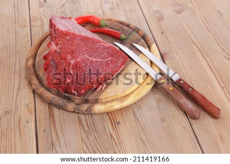 fresh raw beef meat steak chunk with red hot pepper on wood with stainless steel knife