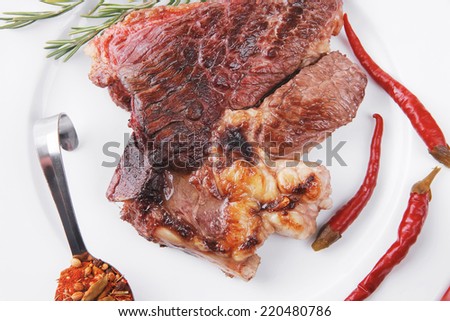meat food : roast beef steak served on white plate with red pepper , spices , and rosemary isolated over white background