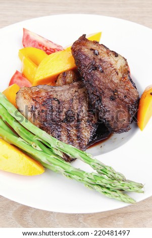 meat food : rare medium roast beef fillet with mango tomatoes and asparagus , served on white dish over wooden table