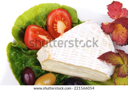 aged camembert cheese on green salad in white platter with olives and tomato isolated over white background