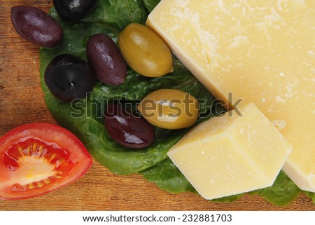 solid parmesan on wooden platter with olives and tomato isolated over white background