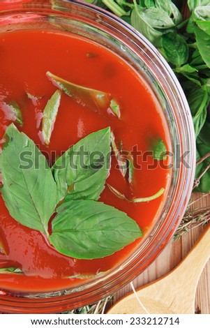 diet food : hot tomato soup with basil thyme and raw tomatoes in transparent bowl over red mat on wood table ready to eat
