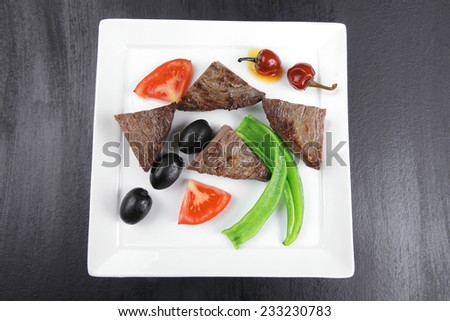 meat food : roast beef fillet mignon served on white plate with apples dill and tomatoes over black wooden table