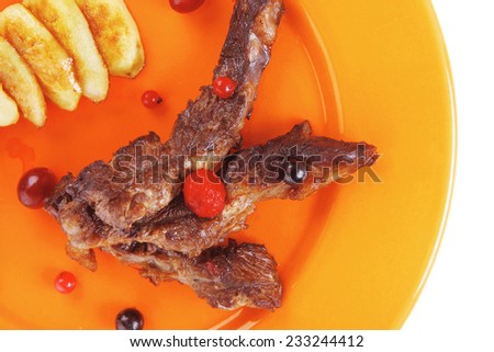 grilled beef meat with berries fried potatoes and cherry under sweet honey sauce on orange plate isolated over white background