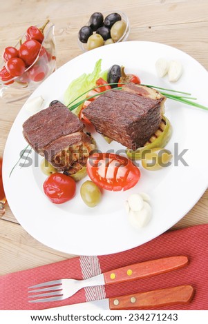 savory food : roast beef garnished with apple juice , green and black olives, red hot peppers on wooden table