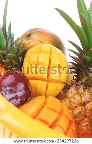 diet food - a lot of fresh raw tropical fruits include pineapple red plum and green mango in orange colander isolated over white background