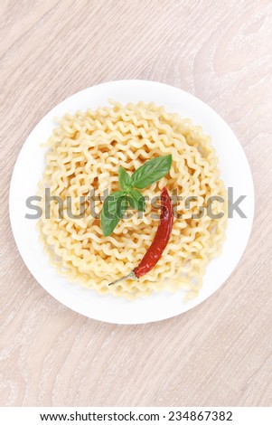 italian food : boiled pasta with basil and red pepper on white dish over wooden table