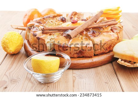 baked food : apple pie served with fresh apples, raw lemon and mandarin,  tea cup on wooden plate over table