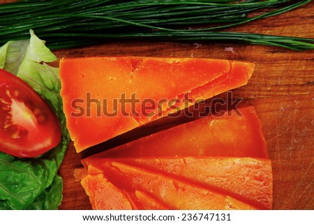 orange aged delicious cheddar cheese chop with slice on wooden plate with tomatoes , chives and salad . isolated over white background