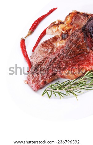 meat food : roast beef steak served on white plate with red pepper , spices , and rosemary isolated over white background