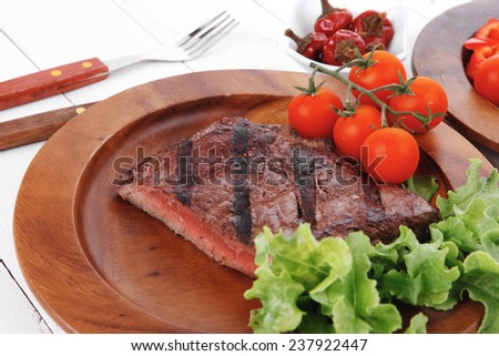 lunch of fresh rich juicy grilled beef meat steak fillet with marks on wooden plate over white table served with vegetable salad and cutlery, new york styled cuisine