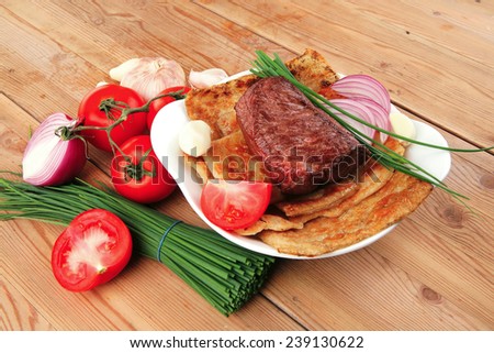 roast meat : beef ( lamb ) steak garnished with onion , tomatoes salad and chives, on wooden table